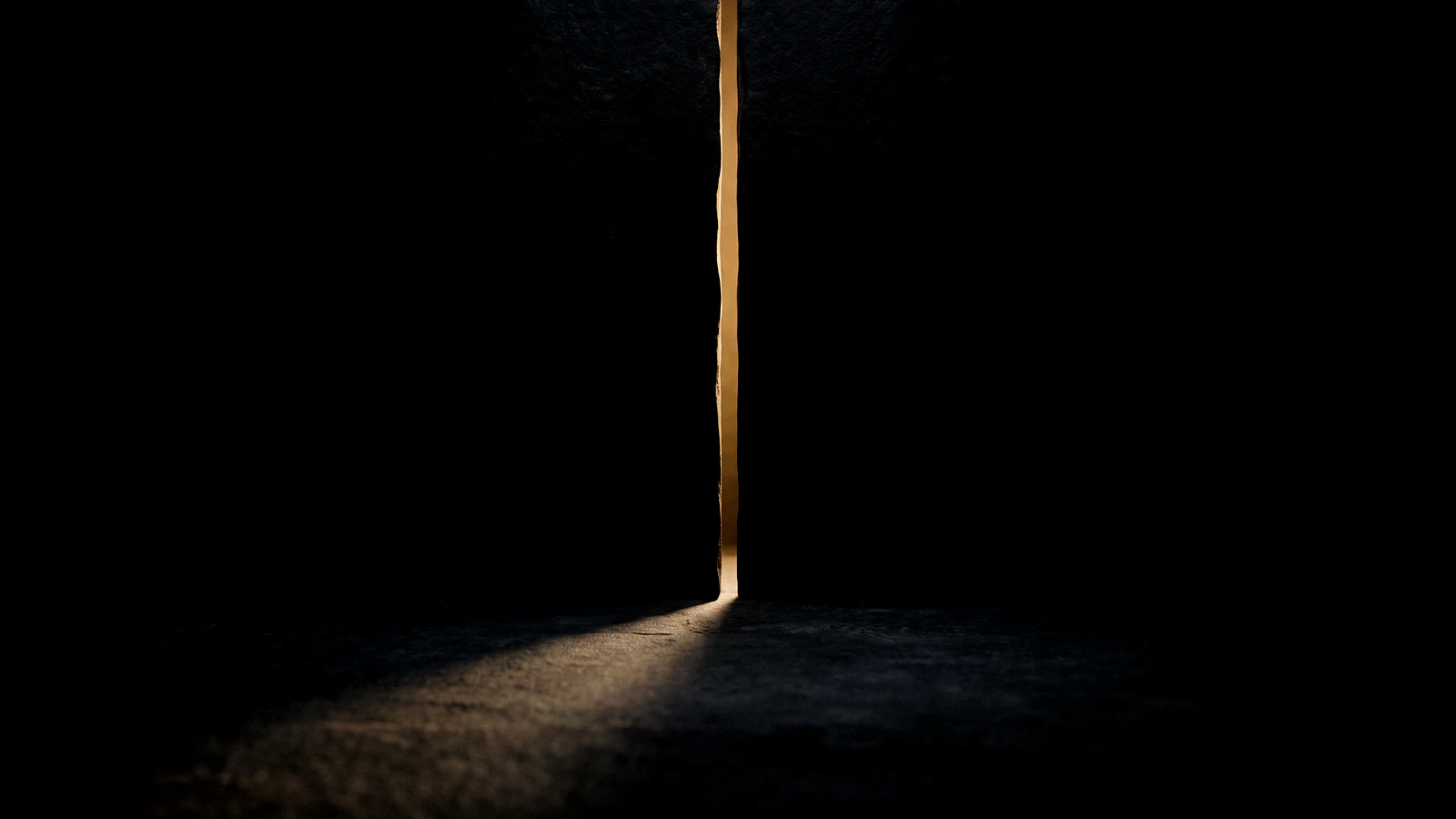 A narrow vertical slit of gold light in a black wall, spilling onto the floor.