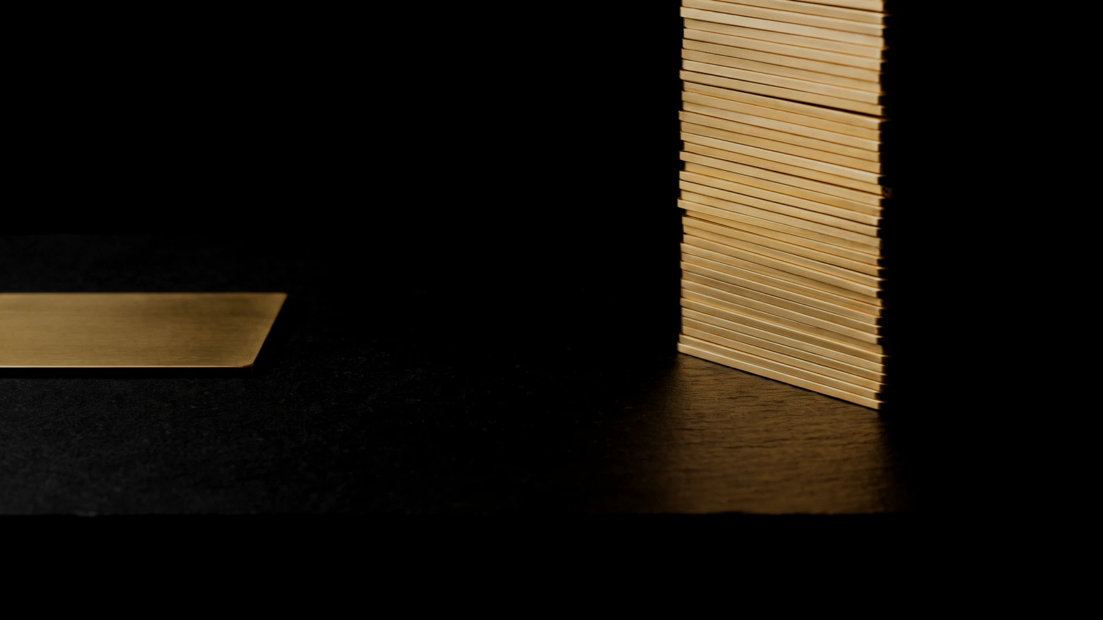 A single flat brass plate on black beside a tall stack of identical plates rising out of frame.