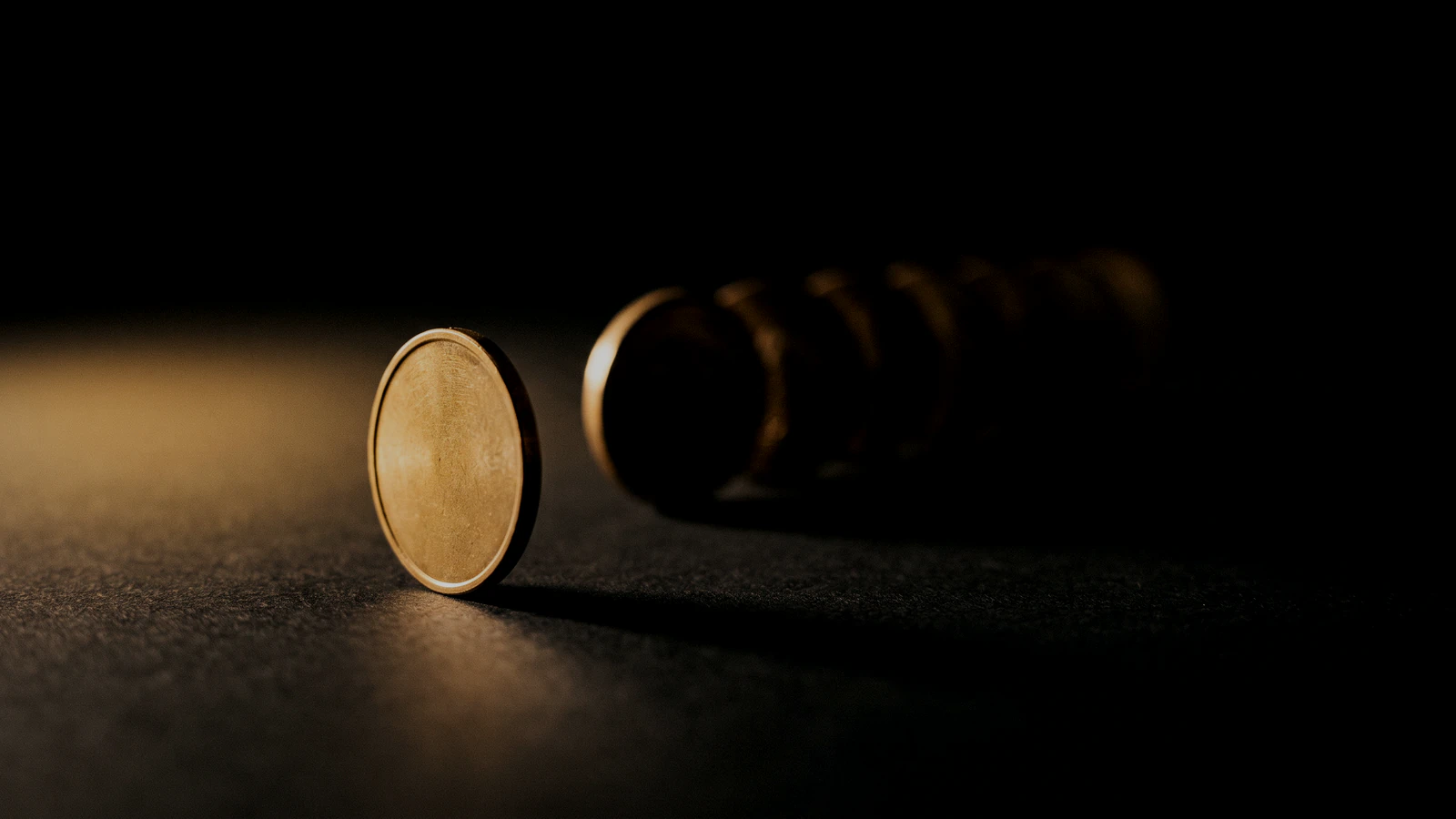 A row of identical brass tokens fading into black, one drawn forward and lit.