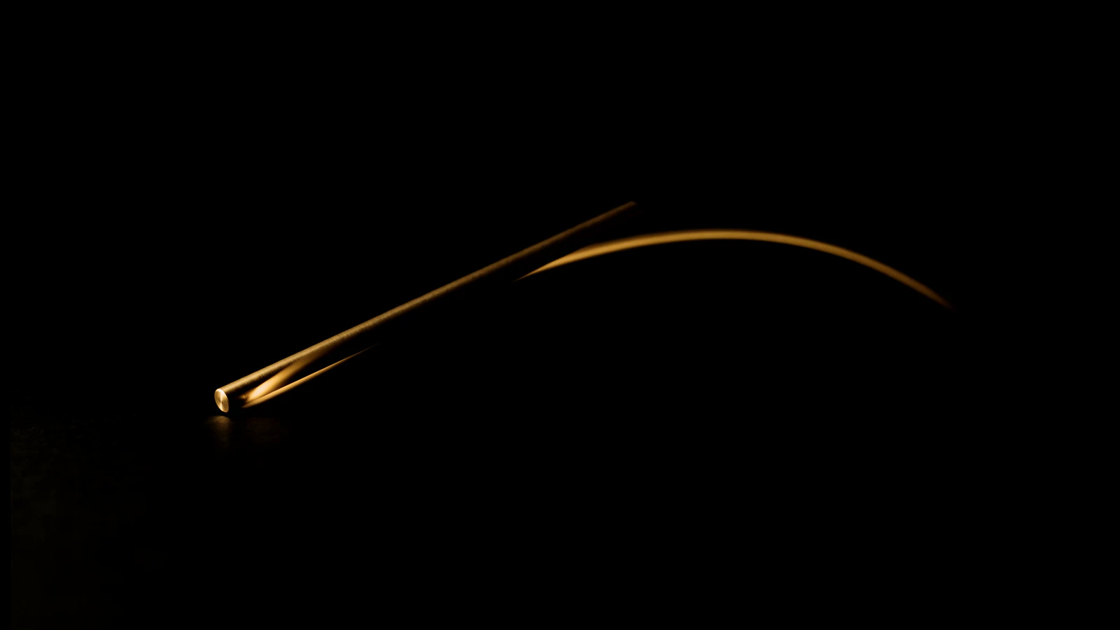 A brass rod in mid-air on black with a curved trail of gold light behind it.